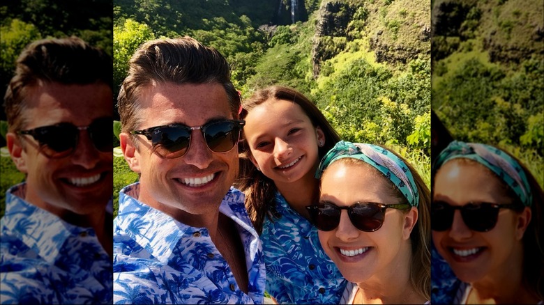 Wes Brown posing with his wife and daughter in front of a green landscape