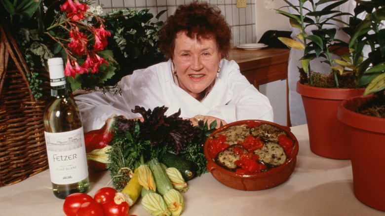 Julia Child poses with a plate of food and wine.
