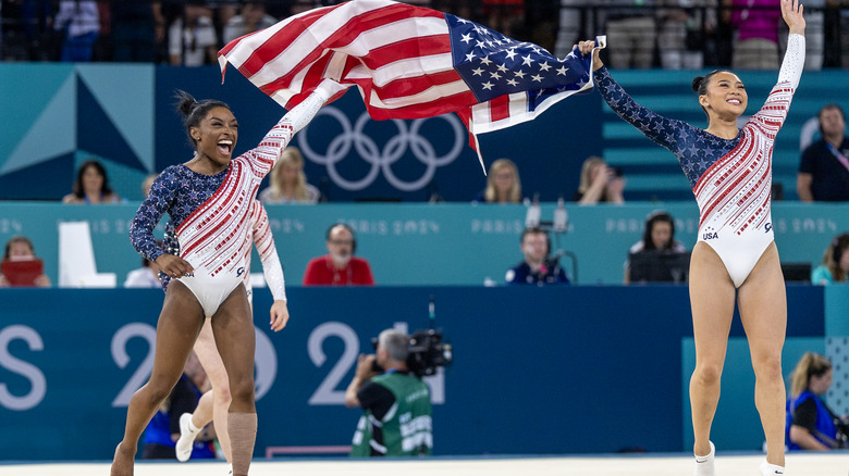 Simone Biles and Suni Lee raising the American flag