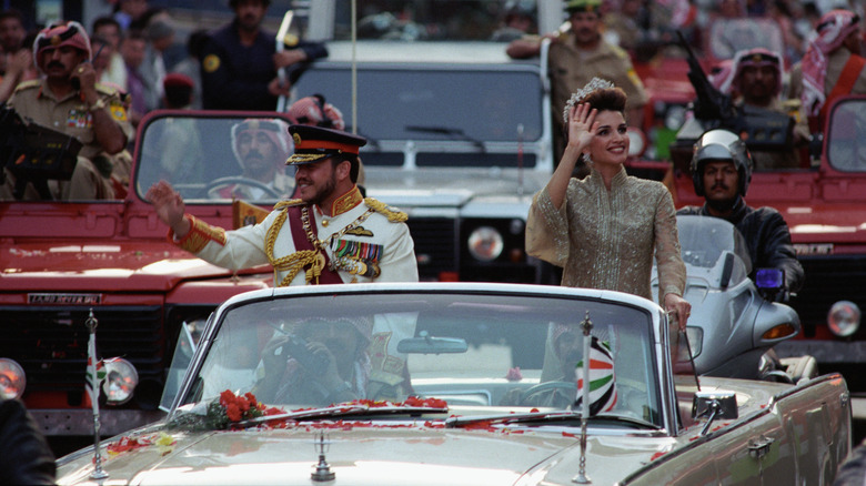 King Abdullah II and Queen Rania wave at crowds from a car 