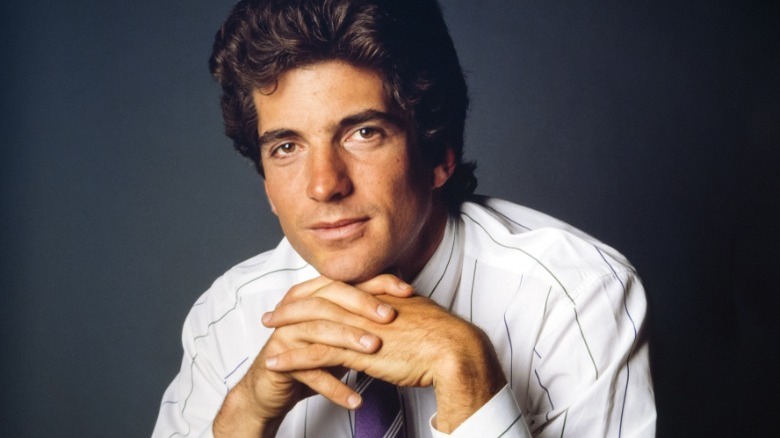 JFK Jr in studio portrait, hands clasped under chin