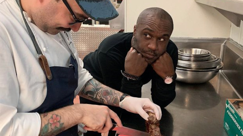 Cliff Crooks looks at another chef as he slices meat.