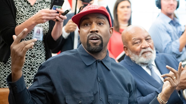 Kanye West gesturing with both hands as he wears "make America great again" cap.