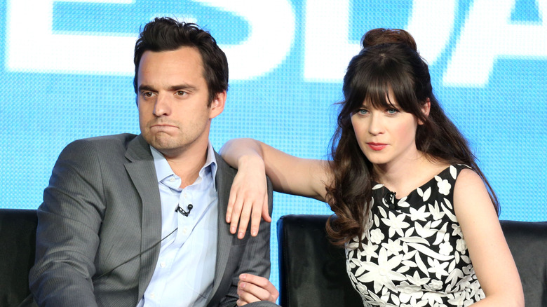 Zooey Deschanel propping her arm on Jake Johnson as they sit together