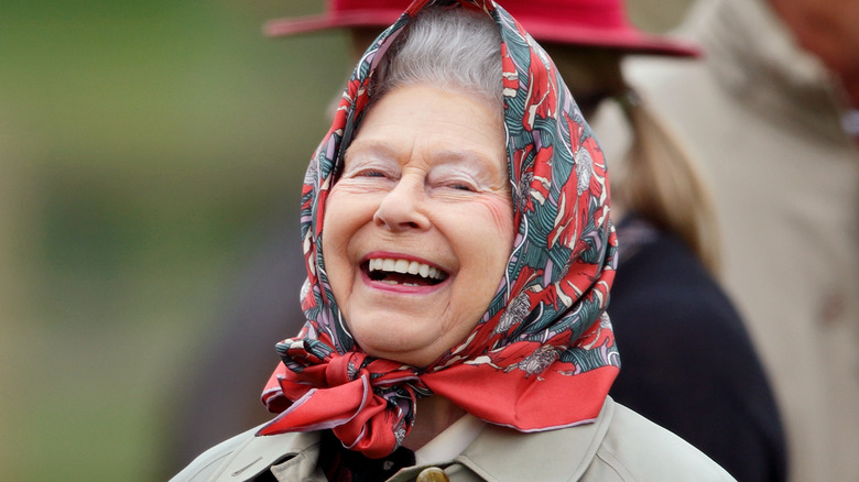 Queen Elizabeth smiling outside with a scarf around her head