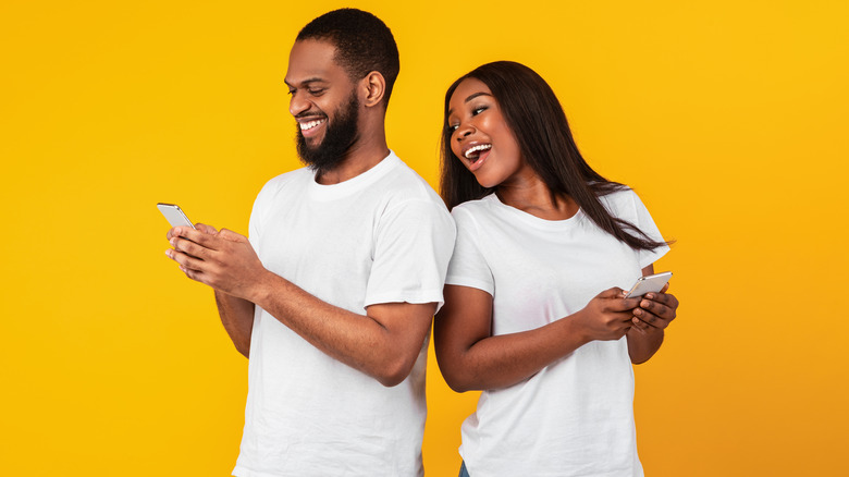 A man and a woman looking at their phones and smiling