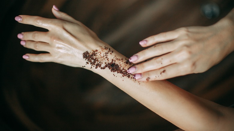 Woman applying a coffee scrub on her arm 