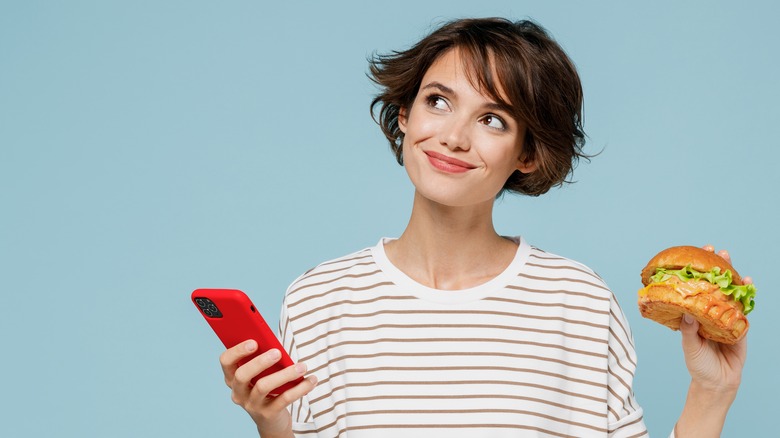 Smiling woman holds a phone and a sandwich