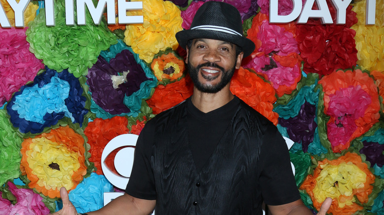 Aaron D. Spears poses on the red carpet wearing a monochrome black outfit and black hat with white band.