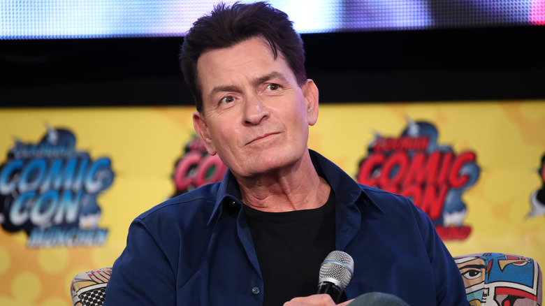 Charlie Sheen sitting on stage with a microphone at Comic Con