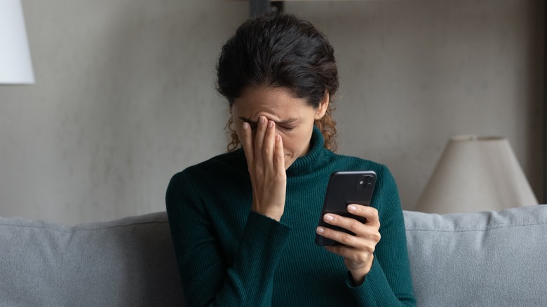 Woman rubs forehead looking at phone