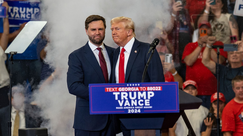 JD Vance and Donald Trump frowning behind a podium