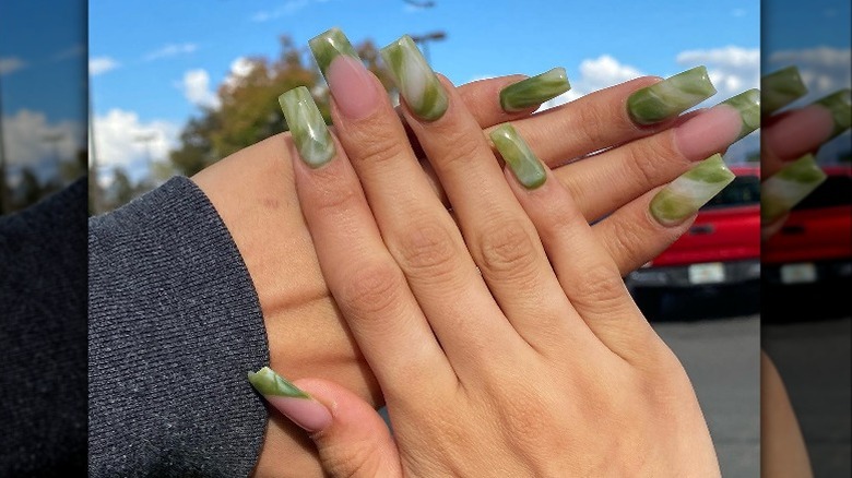 Hands showing off green marble nail art in parking lot