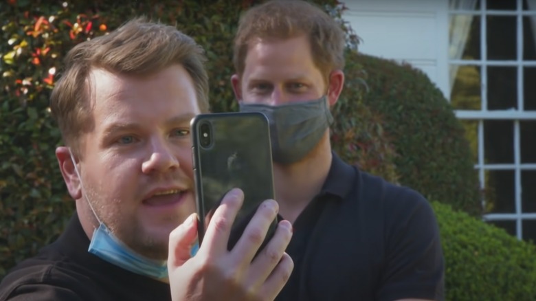 James Corden smiling with phone and Prince Harry