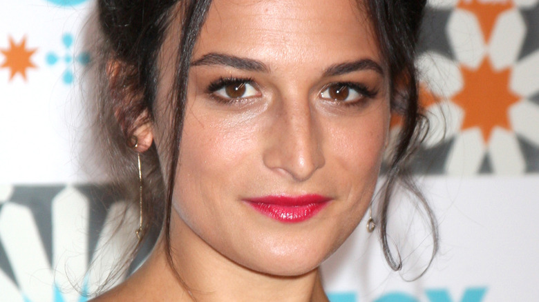 Jenny Slate smiling wearing hoop earrings and red lipstick