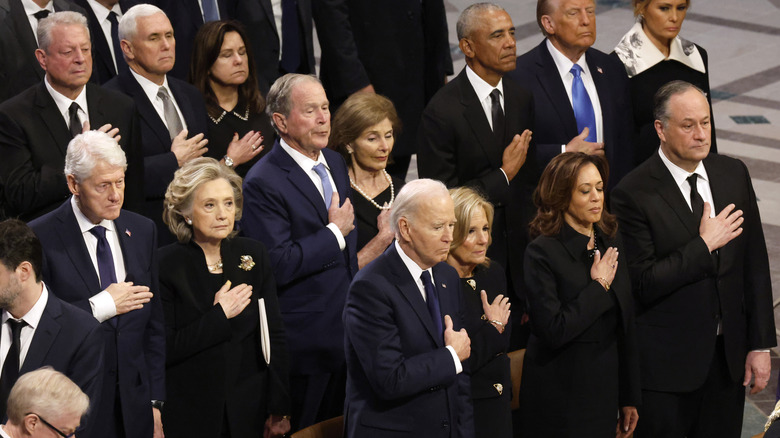 Several public officials, including Jill Biden and Donald Trump stand with their hand across their chest at President Jimmy Carter's funeral