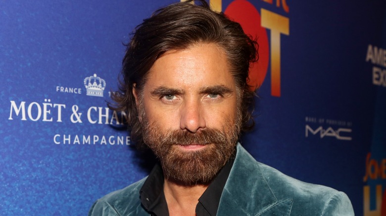 John Stamos with a beard in front of blue backdrop