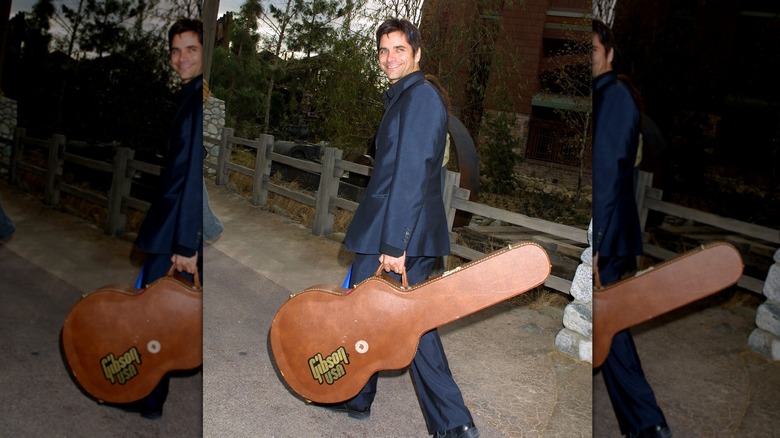 John Stamos carrying a guitar