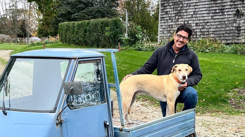 Jonathan Knight standing in front of old barn with dog and work truck