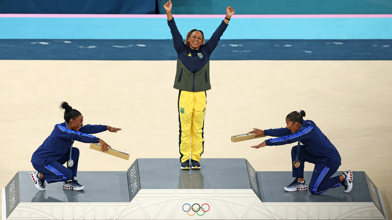 Simone Biles and Jordan Chiles bow to Rebeca Andrade on the medal podium