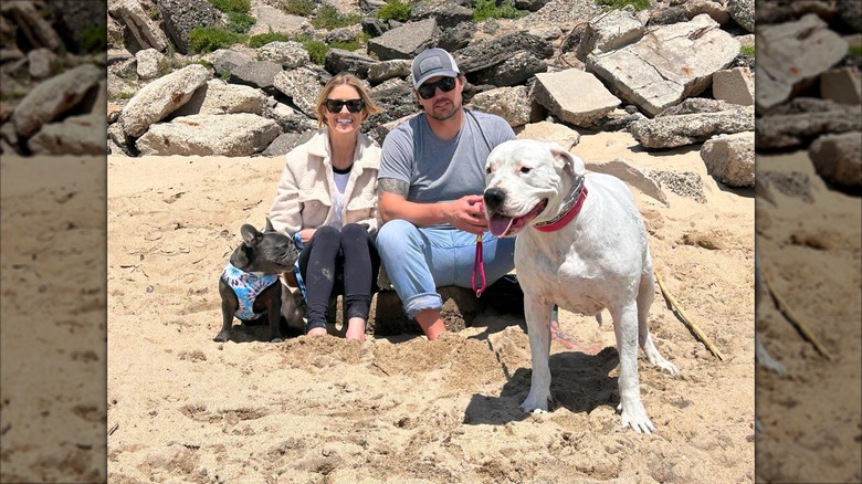 Christina and Josh Hall sitting on the beach with their two dogs