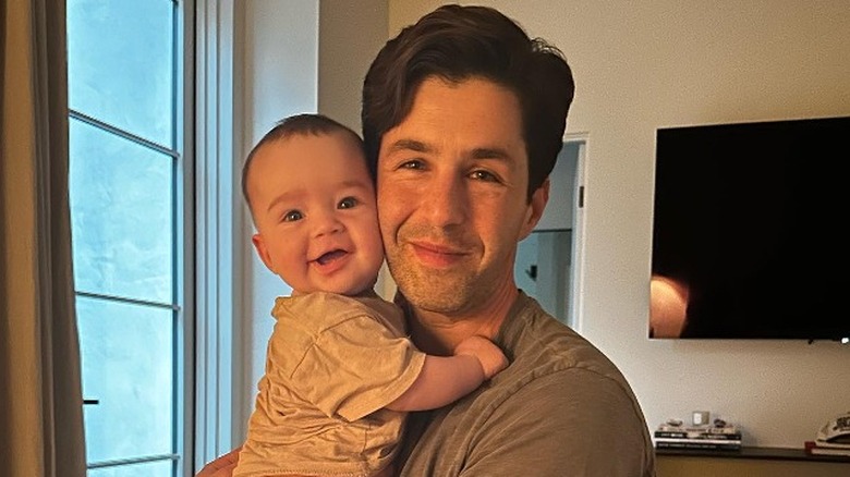 Peck smiling holding newborn son