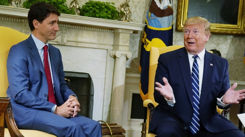 Justin Trudeau sitting with his hands folded in his lap, listening to Donald Trump animatedly speak