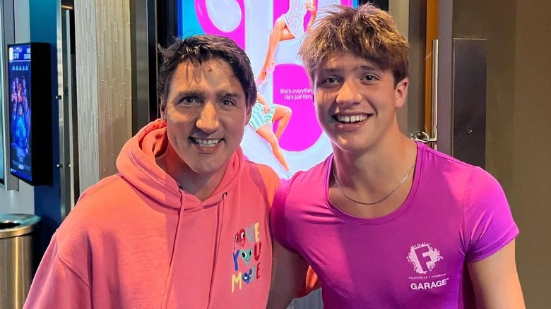 Justin Trudeau and son Xavier wearing pink tops, posing in front of a poster for the Barbie movie