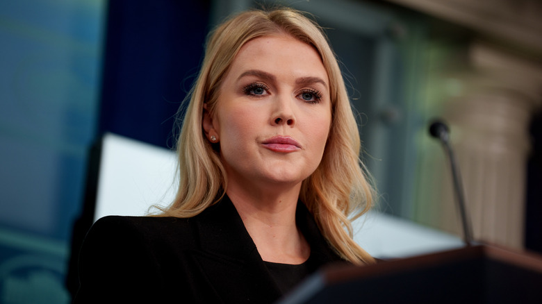 Karoline Leavitt in a black suit speaks on a podium