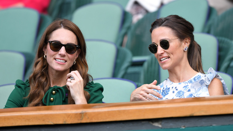 Kate and Pippa Middleton sit side by side while wearing sunglasses