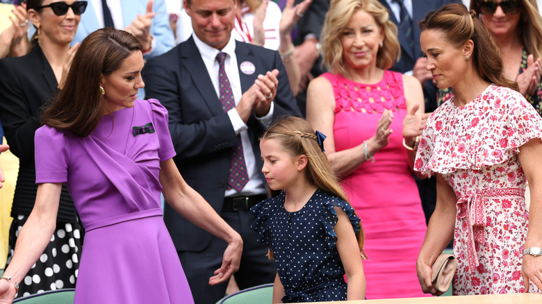 Kate Middleton and Pippa Middleton stand, looking at Princess Charlotte