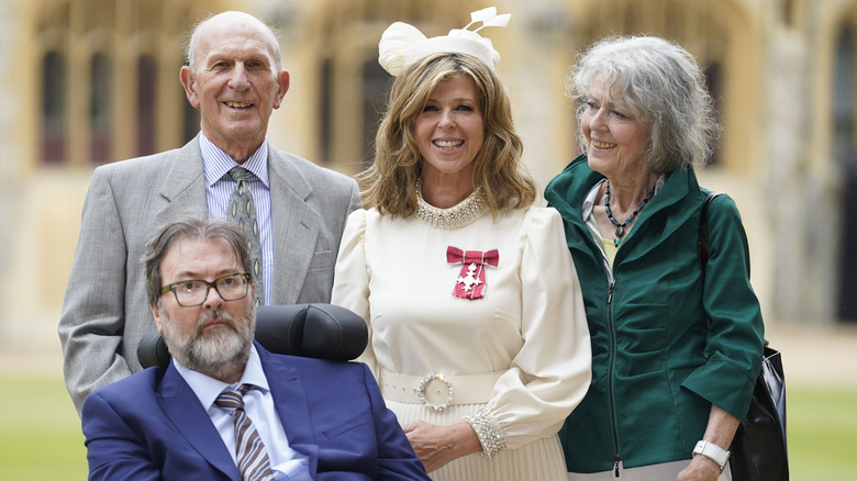 Kate Garraway smiling with Derek Draper and her parents after receiving her MBE 