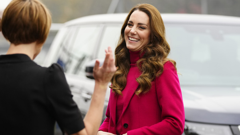 Kate Middleton laughing in a fuchsia top and coat 