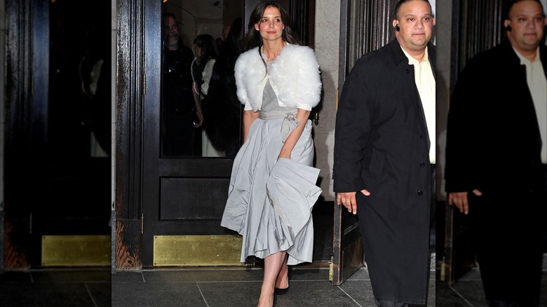 Katie Holmes walking in a gray skirt and top with a white bolero