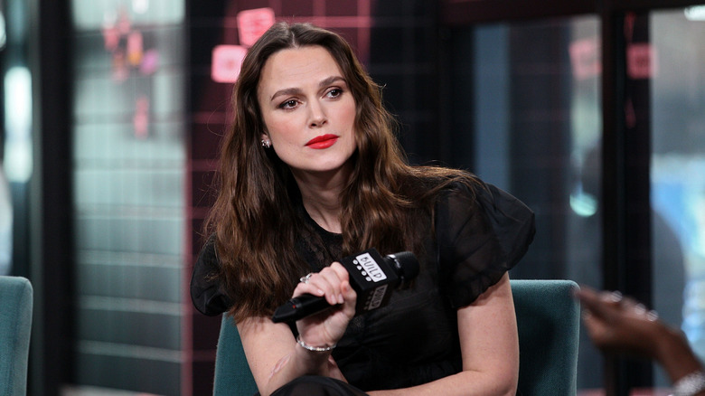 Keira Knightley holding a microphone in a black dress