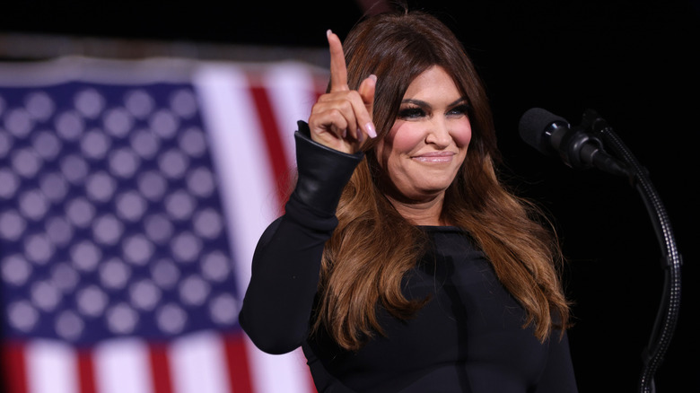 Kimberly Guilfoyle pointing to the sky in front of American flag