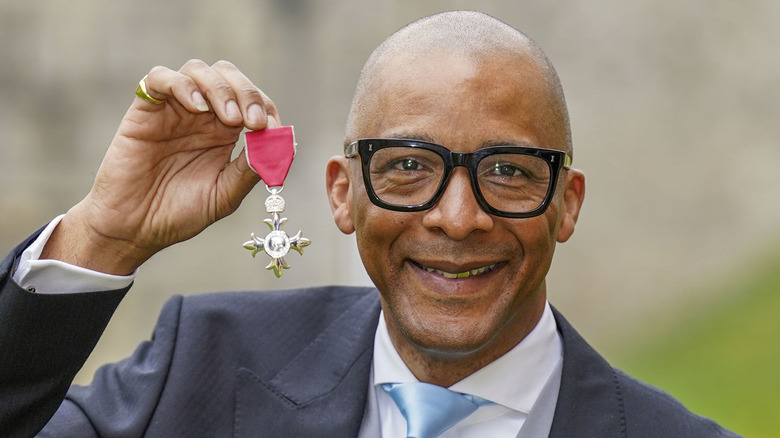 Jay Blades smiling and holding up MBE honor