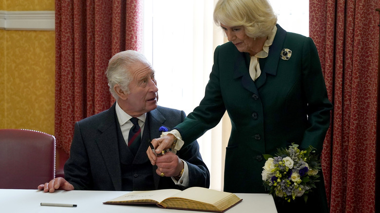 King Charles signing a visitor's book in Scotland with Camilla, Queen Consort