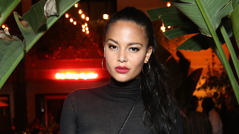 Kyra Green in black turtleneck in front of green plants