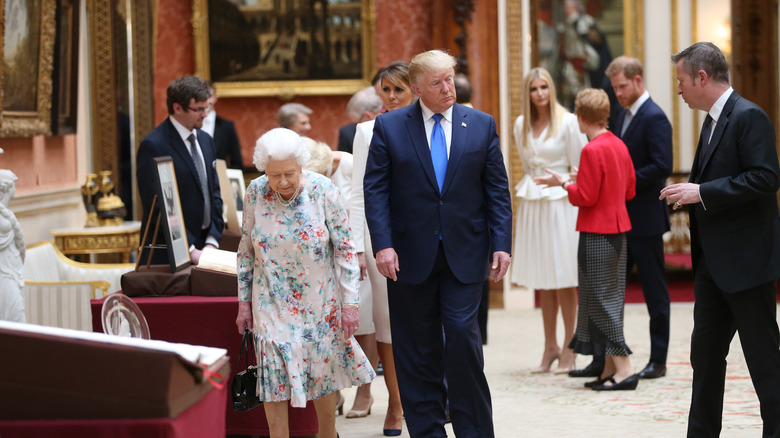 Donald Trump stands near Queen Elizabeth III; Prince Harry stands in the background