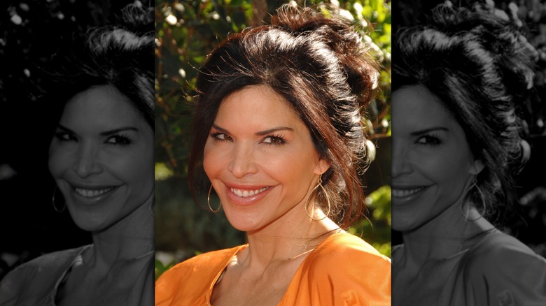 Lauren Sanchez smiling, standing in front of foliage, wearing orange top