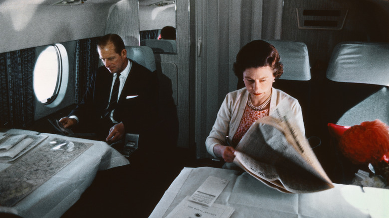 Queen Elizabeth and Prince Philip reading newspapers on a plane