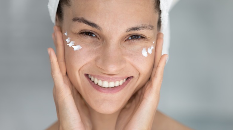 Woman smiling while applying makeup primer