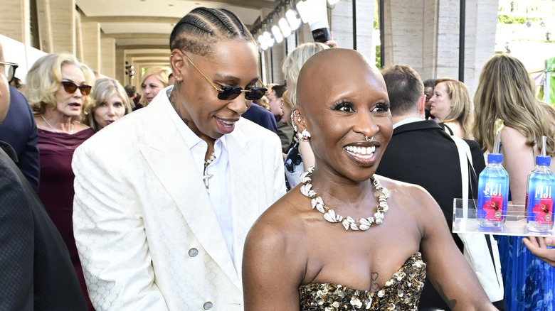 Cynthia Erivo smiles while Lena Waithe holds her dress