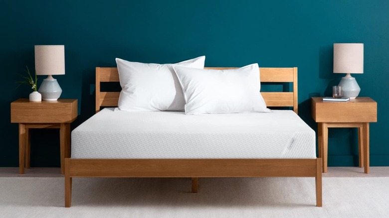 white tuft & needle mattress on a wood bed frame in front of a dark teal wall