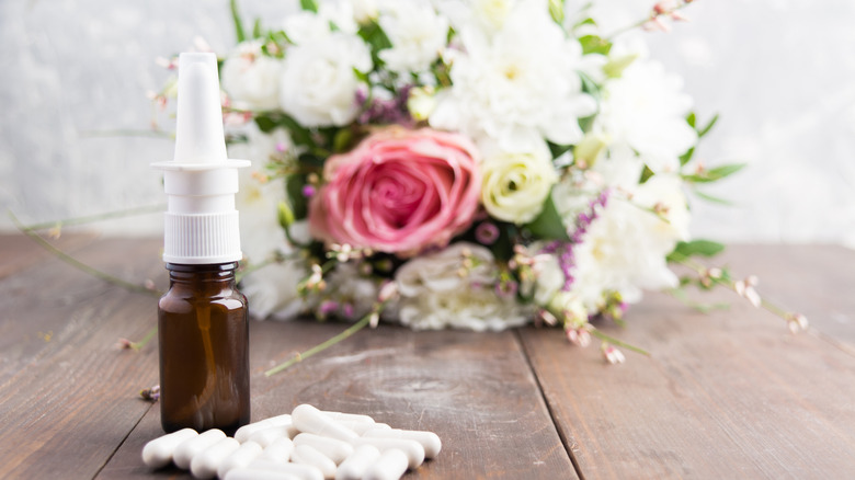 allergy medicine pills and nasal spray in front of bouquet of flowers