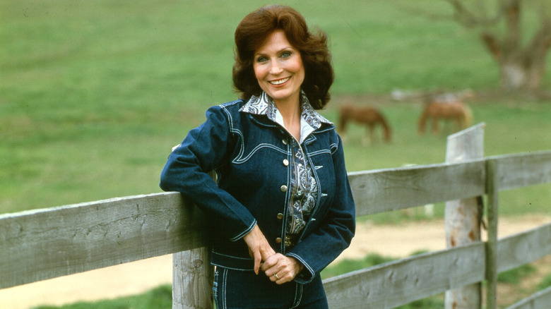 loretta lynn leans on a fence in 1972 portrait, horses in background