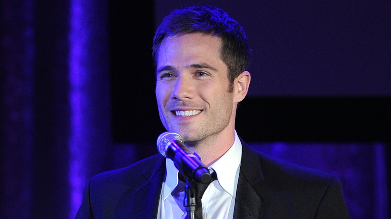 Luke Macfarlane smiling in front of a microphone