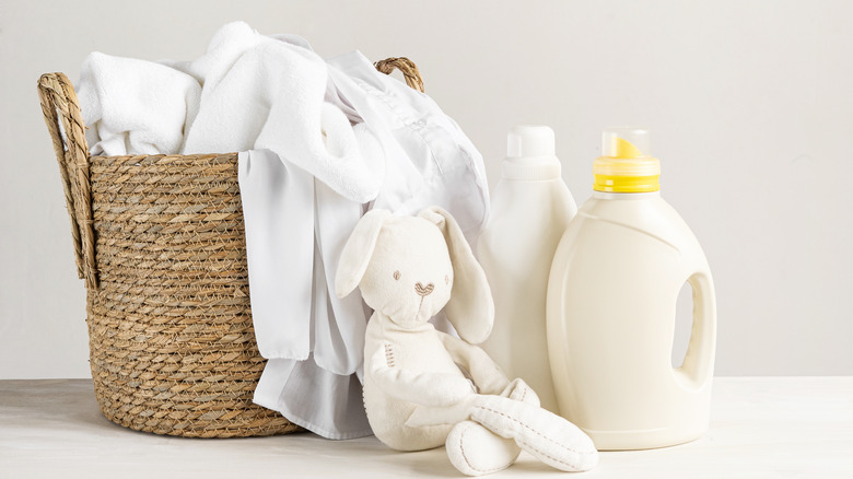 A basket with bed sheets next to a stuffed bunny and two detergent bottles