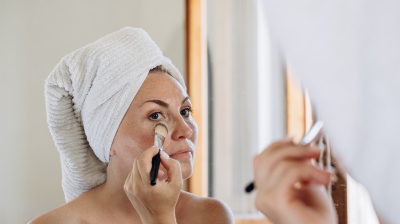 Woman with head towel applying makeup in the mirror